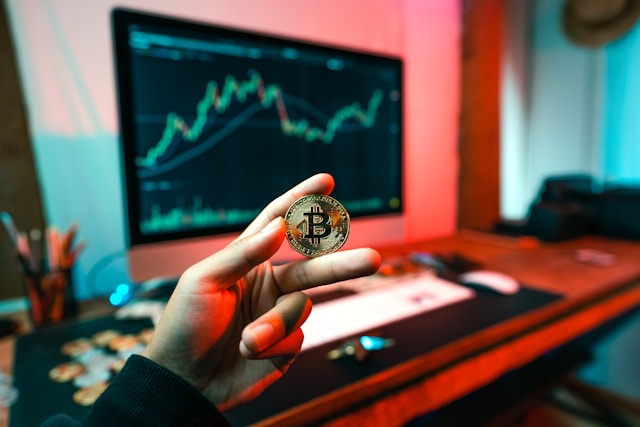 holding bitcoin in front of computer screen